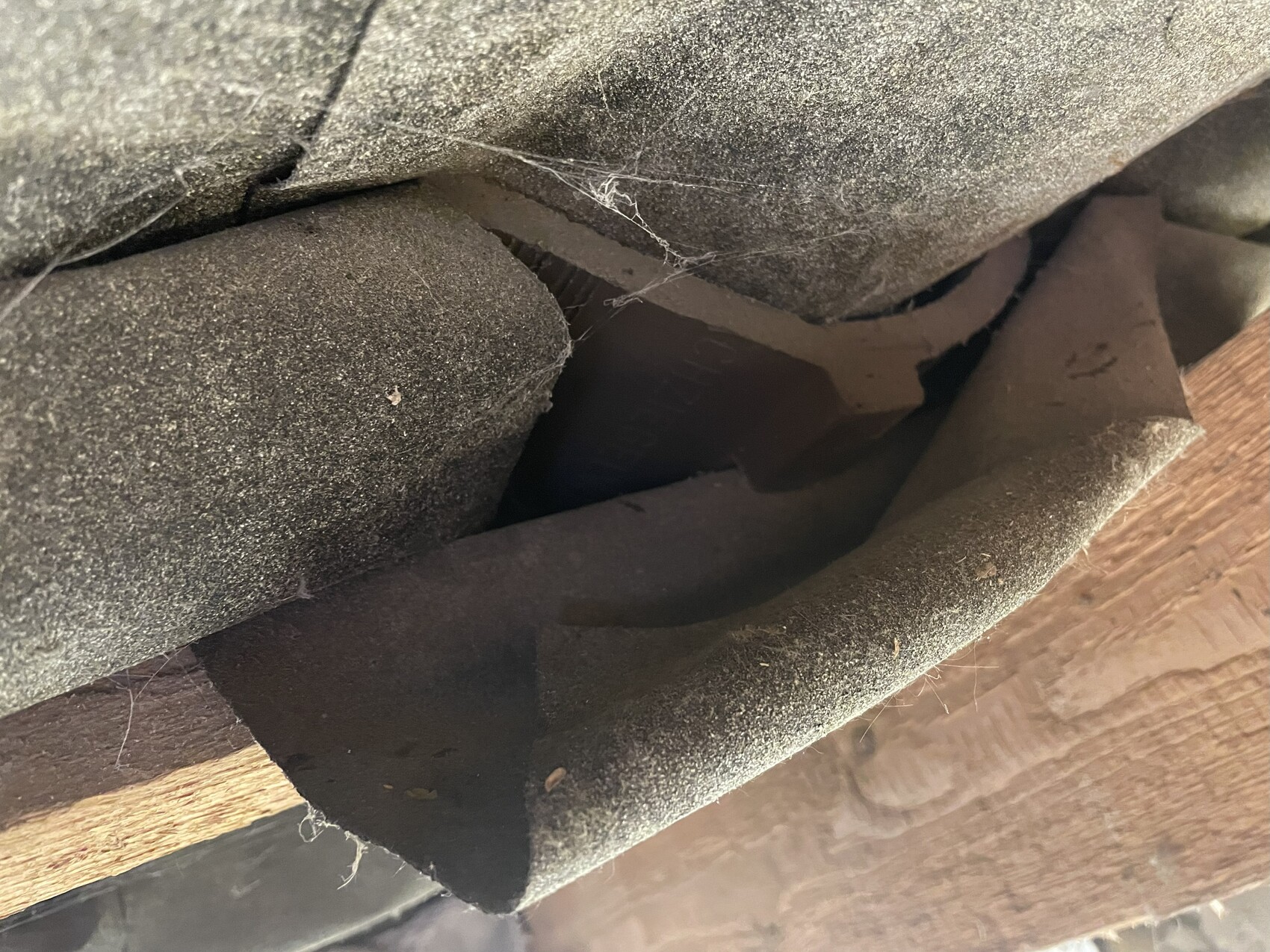 Nahaufnahme von staubiger Dachpappe und Holzbalken in einer Dachkonstruktion.