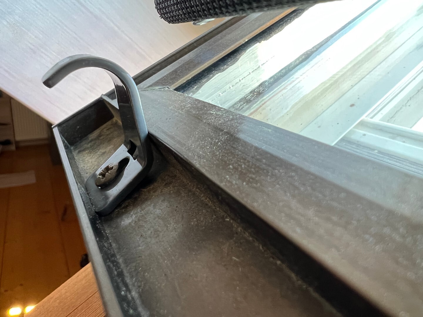 Nahaufnahme eines gebogenen Fenstergriffs am Metallrahmen, staubig.