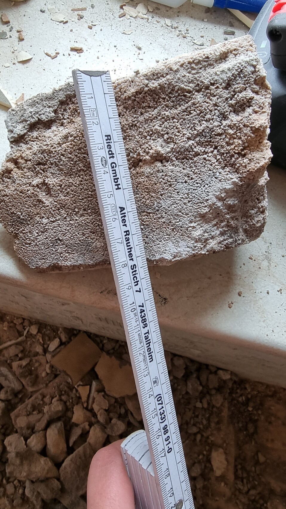 Grober Betonblock mit diagonalem Maßband darauf auf einer Baustelle, ca. 20 cm.