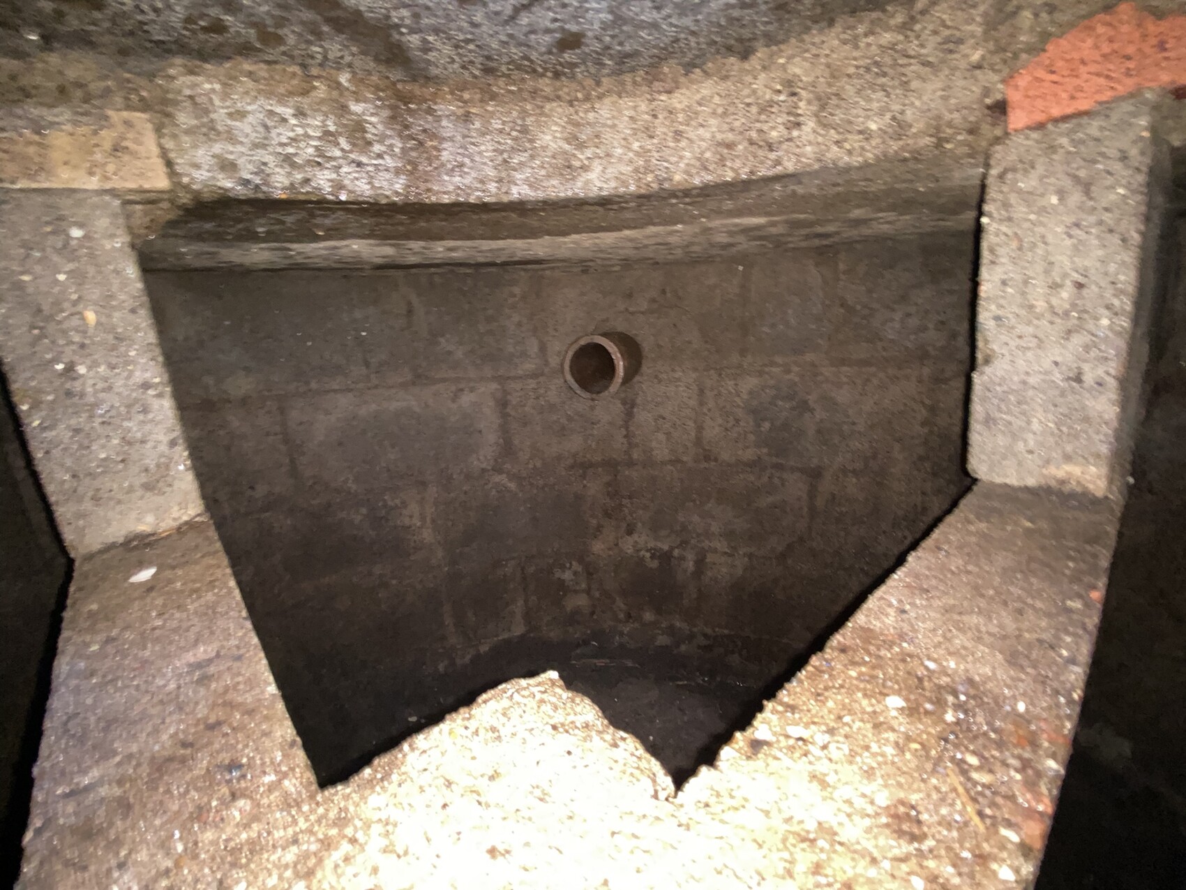 Innenansicht eines Beton-Schachts mit zentralem runden Abflussrohr, von Steinblöcken umrahmt.