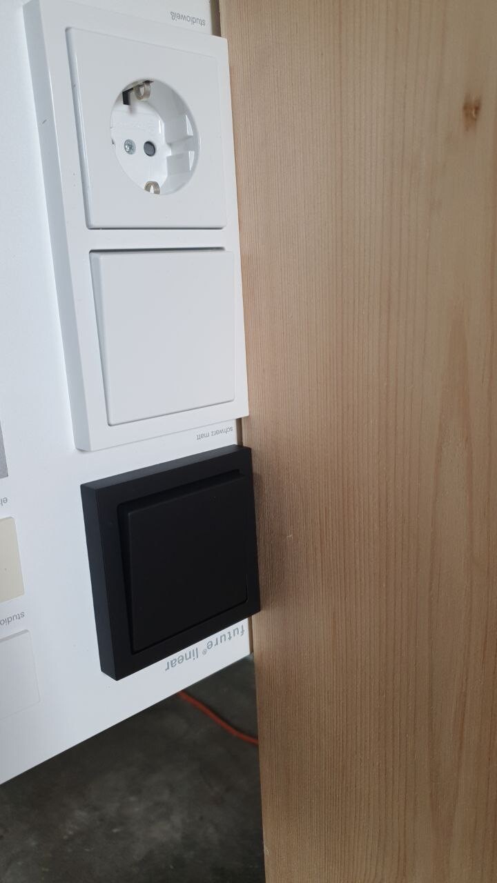 Weißes Steckdosen- und Lichtschalter-Panel an Wandplatte; obere Steckdose, unterer schwarzer Schalter.