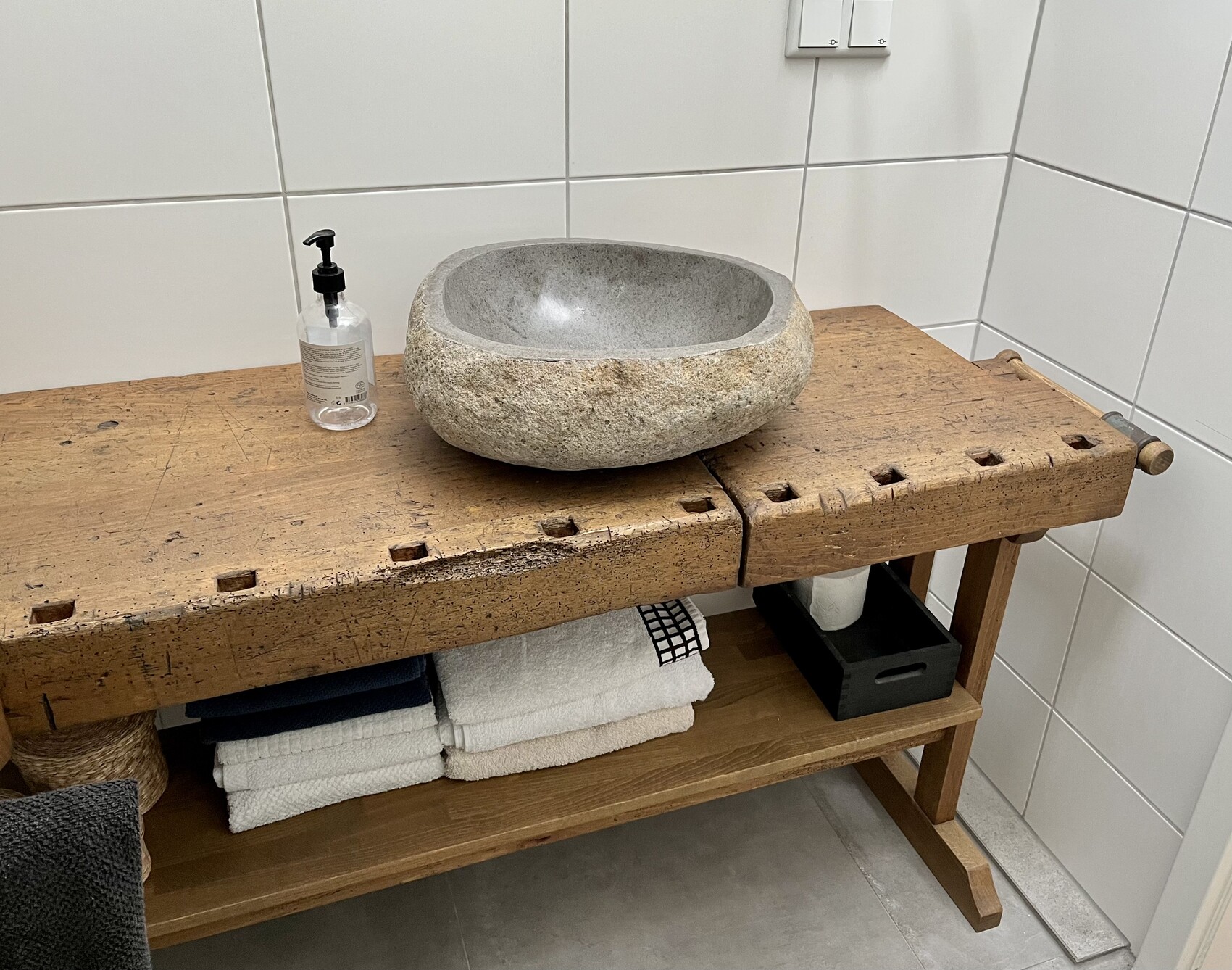 Rundes Stein-Becken auf einer rustikalen Holzbank, Seifenspender und gefaltete Handtücher daneben.