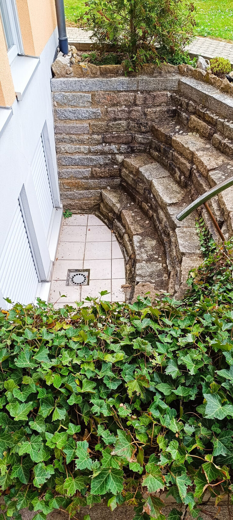 Stufen aus Stein bilden eine Halbkreis-Treppe neben Haus, von Efeu umrankt.