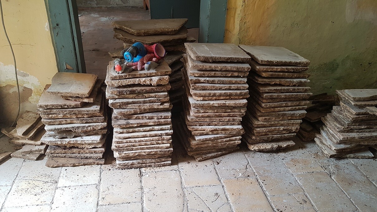 Mehrere Stapel Steinbodenplatten auf einer Baustelle, staubig und rauer Untergrund