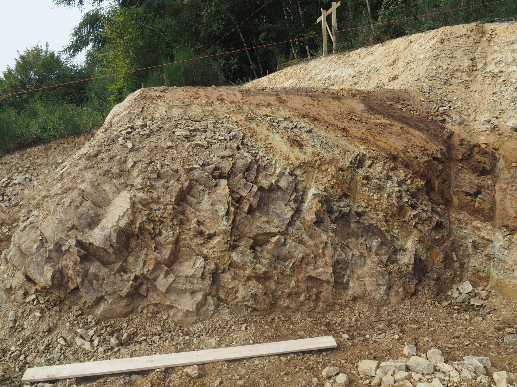 Aufgerissener Erd- und Felswall an einer Baustelle, rotes Absperrband, Holzpfosten, Geröll