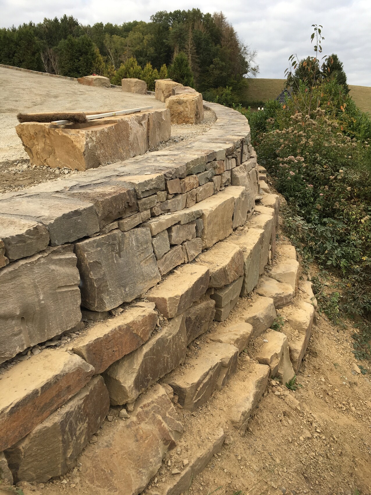 Steinmauer mit terrassierten Stufen am Hang, Kiesweg und Gartenpflanzen