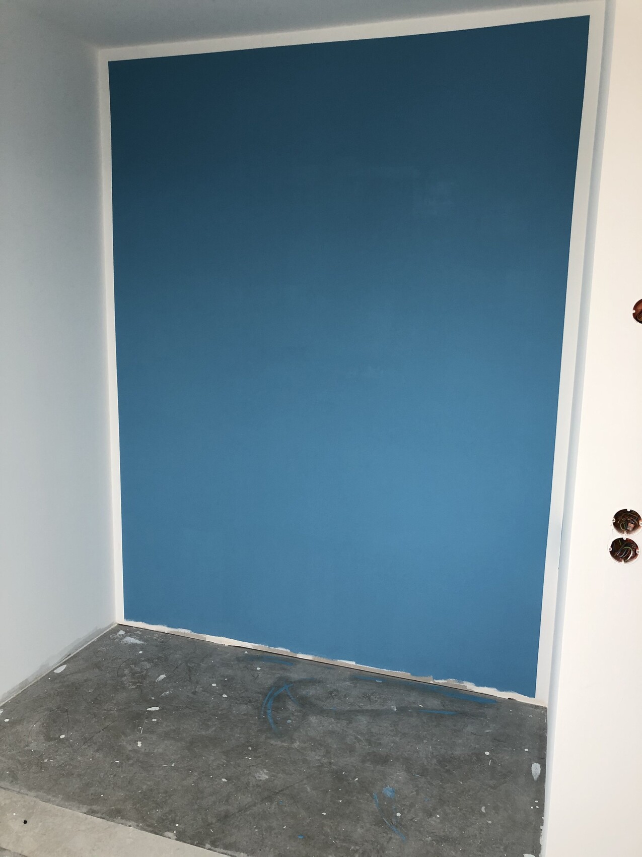 Blaue Wand in renovierter Ecke, weißer Rahmen, Boden mit Farbflecken.