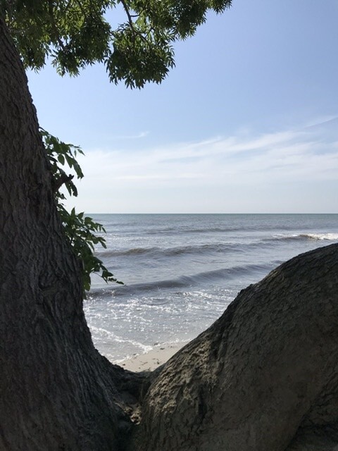 Strand zwischen zwei Felsbrocken mit Meer, Sand und blauem Himmel.