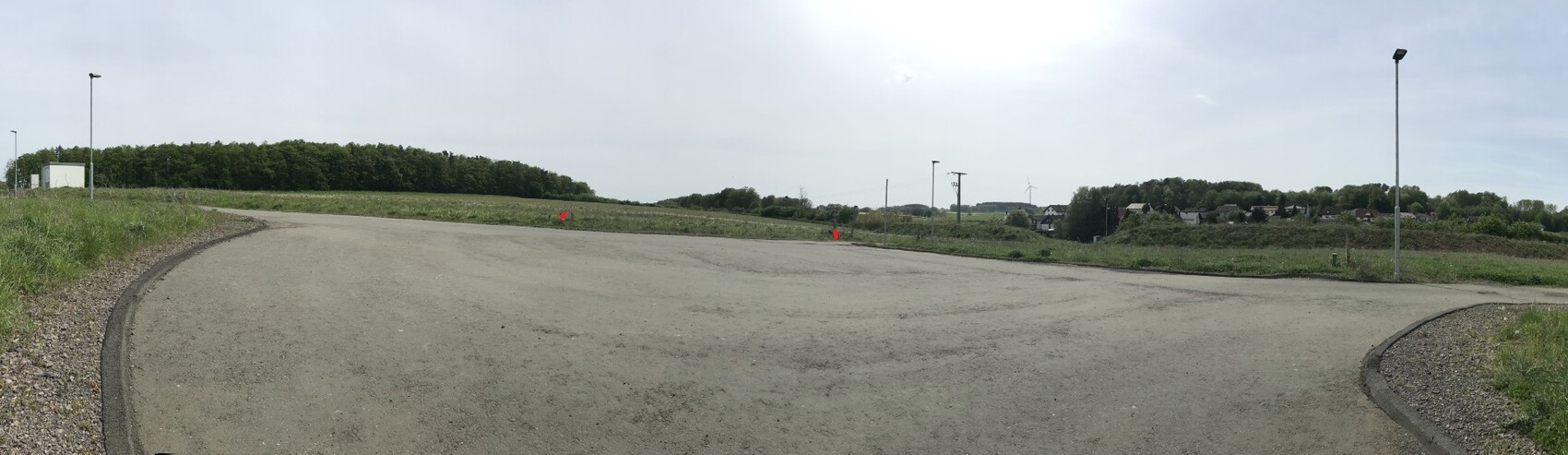 Panorama einer leeren Asphaltkreuzung in ländlicher Umgebung mit Bäumen, Häusern und Windrad.