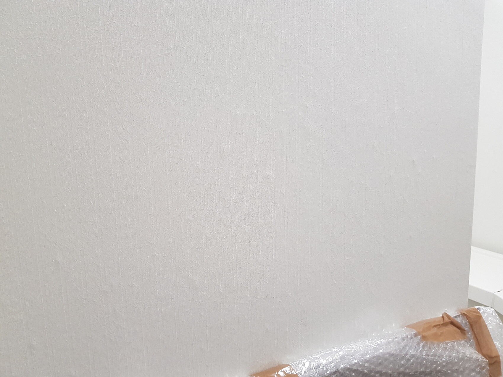 Weiße, strukturierte Wand; unten rechts liegen Luftpolsterfolie und braunes Klebeband.