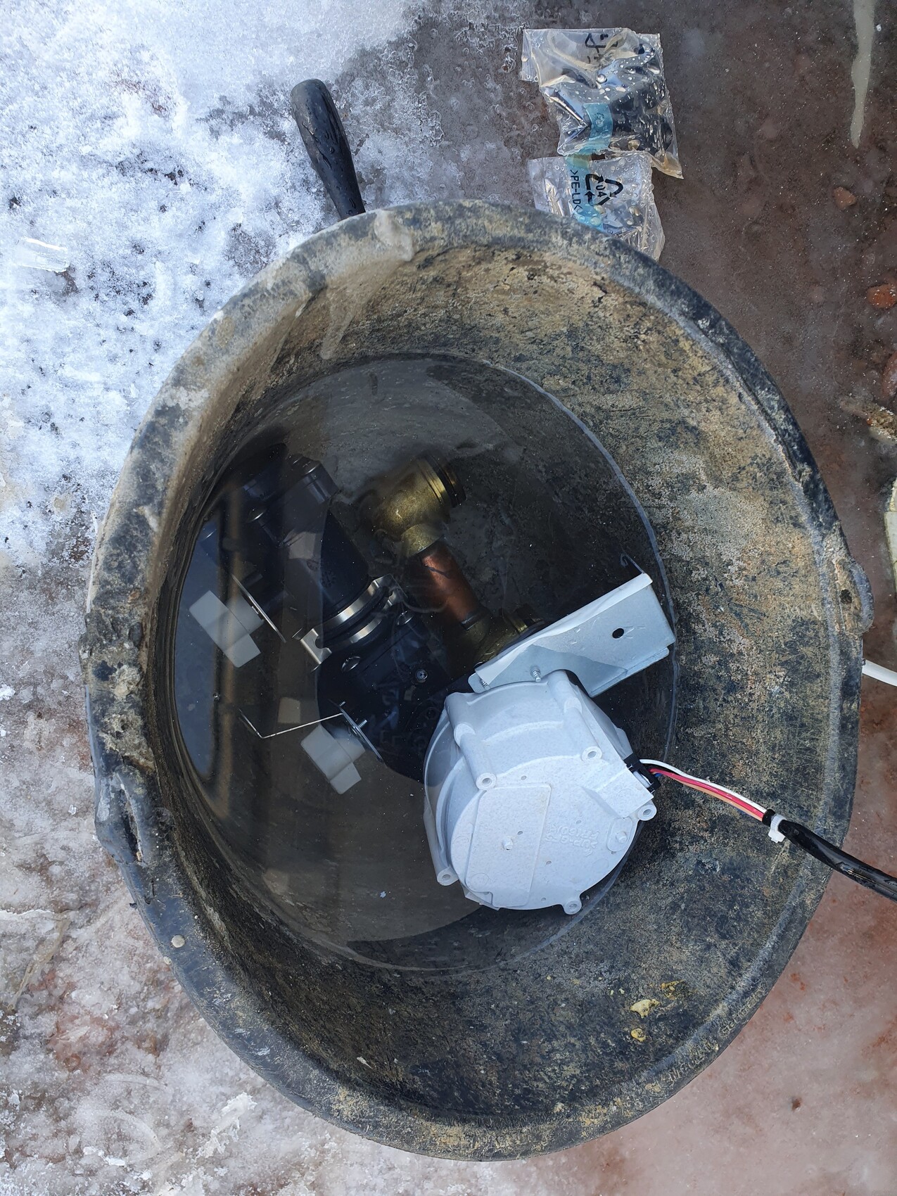 Runder Betonschacht mit installierter Unterwasserpumpe, Motorgehäuse und Kabeln.