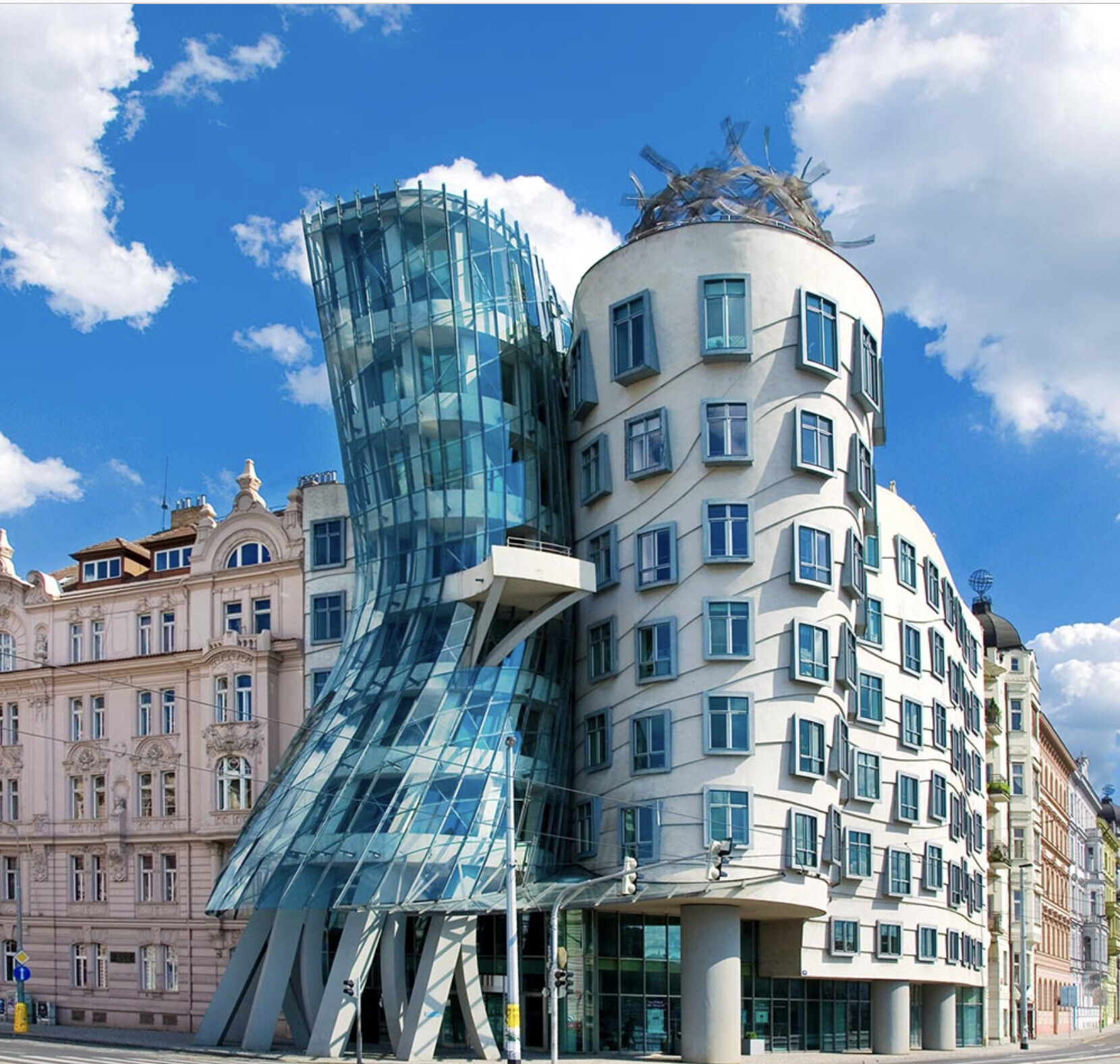 Modernes, geschwungenes Glasgebäude neben historischen Pastellfassaden in Prag.