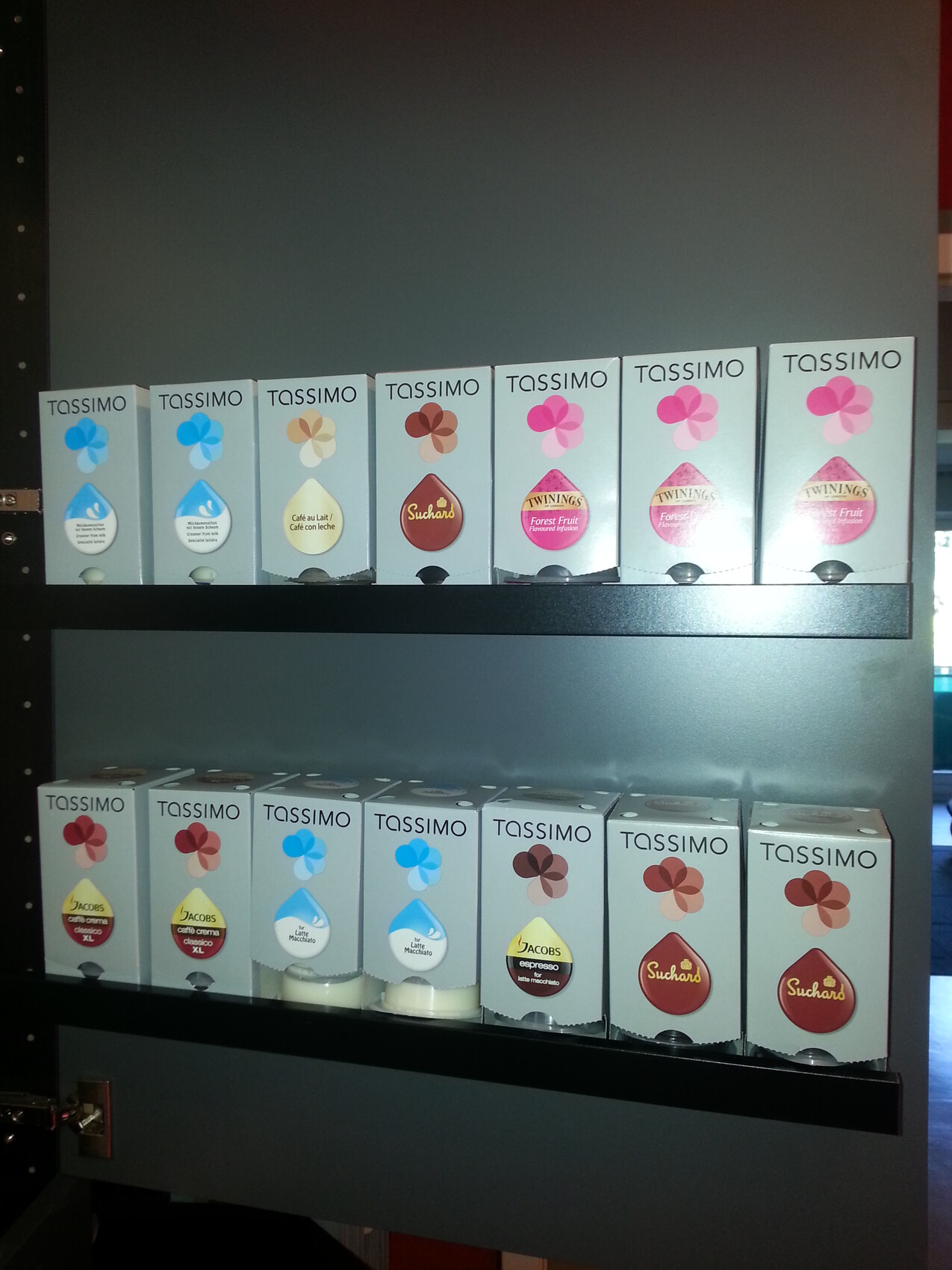 Regal mit Tassimo Kapseln in unterschiedlichen Sorten auf zwei Ebenen.