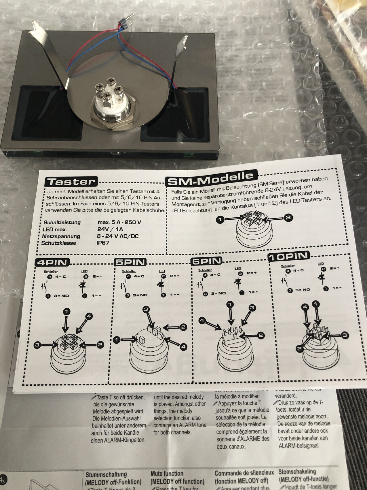 LED-Taster-Modul mit Mehrpin-Stecker auf schwarzer Platte; Drahtanschlüsse und Anleitung sichtbar.