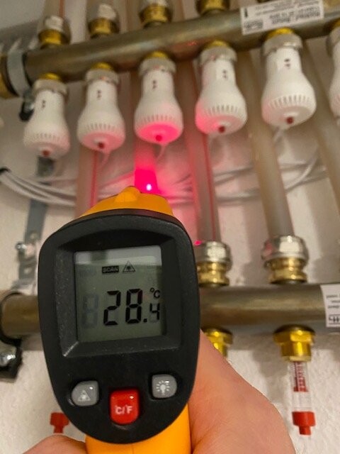 Infrarot-Thermometer misst Temperatur vor Heizungsrohren; Anzeige ca. 28 °C.