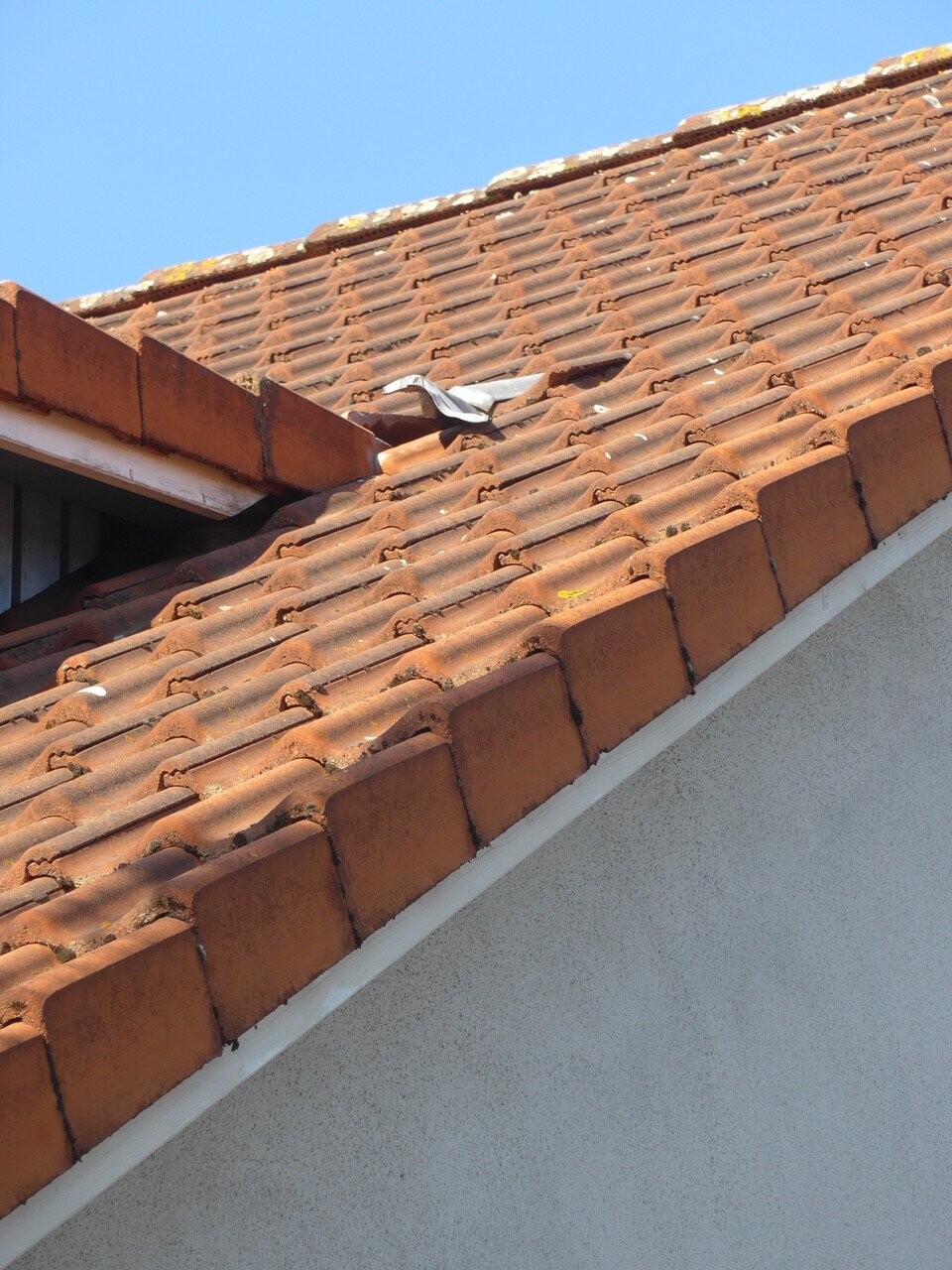 Dach mit orange-braunen Tonziegeln; silbern glänzende Folie liegt auf Ziegeln, blauer Himmel.