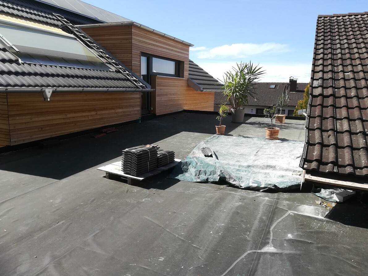 Dachterrasse mit Holzverkleidung, Topfpflanzen und Paletten mit Dachziegeln.