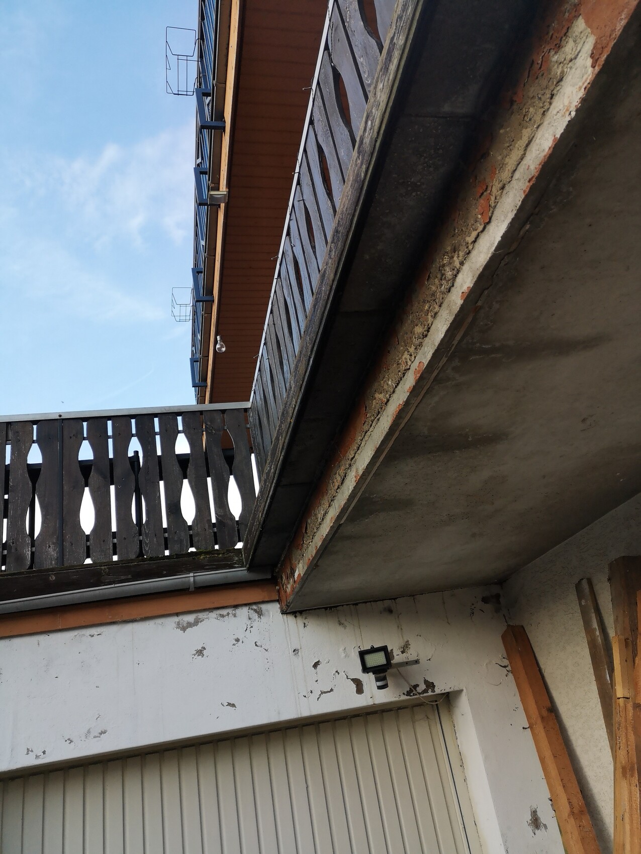 Außenaufnahme eines Gebäudes: Balkon mit dunklem Holzgeländer, blaue Fassade, Betonunterzug.