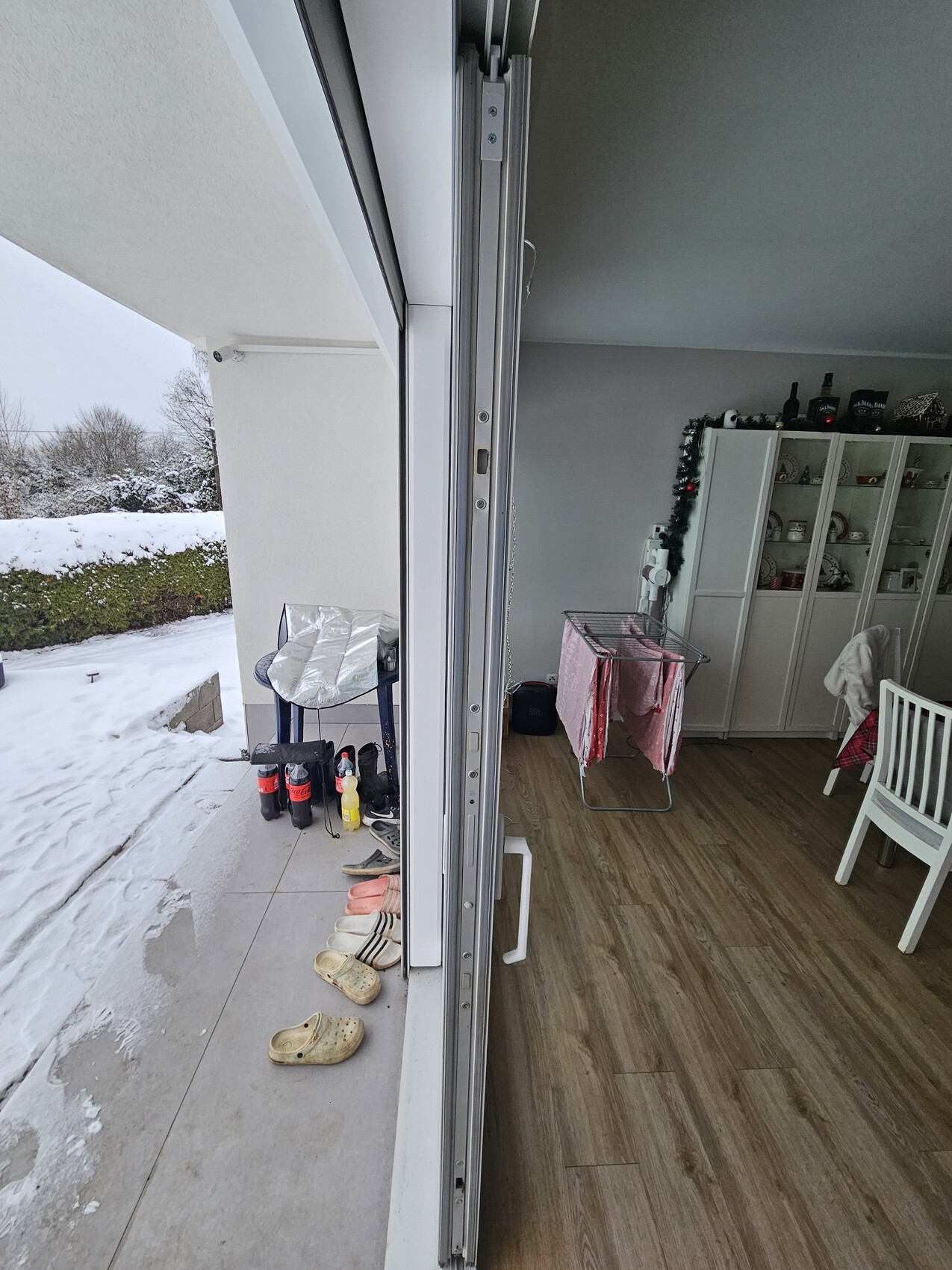 Offene Balkontür führt ins Wohnzimmer mit Laminatboden; verschneiter Balkon, Schuhe sichtbar