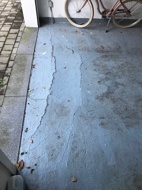 Außenbereich: blau gestrichener, rissiger Betonboden; im Hintergrund ein Fahrrad angelehnt.