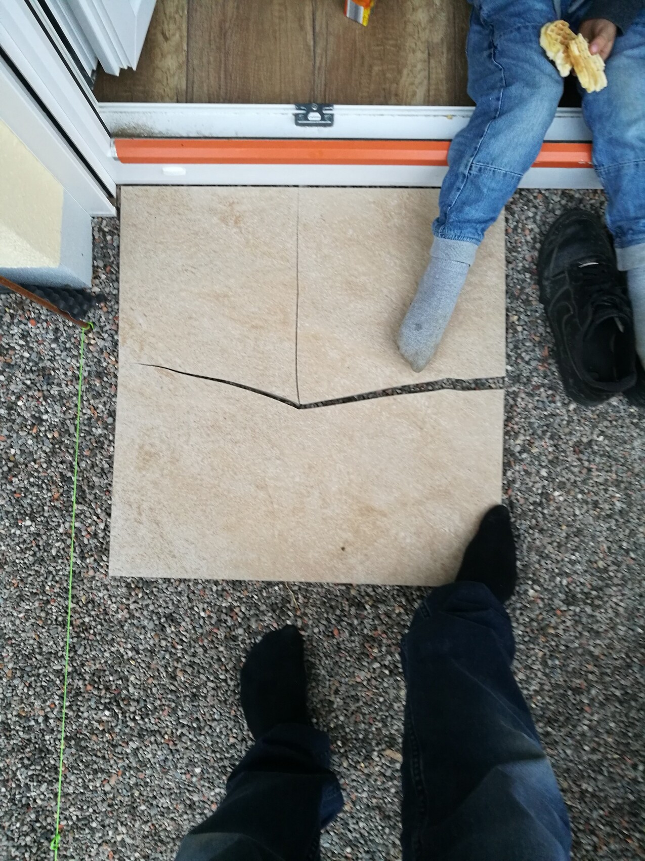 Außenbereich vor Haustür mit beigen Fliesen, Person steht am Eingang, grüne Schnur am Boden