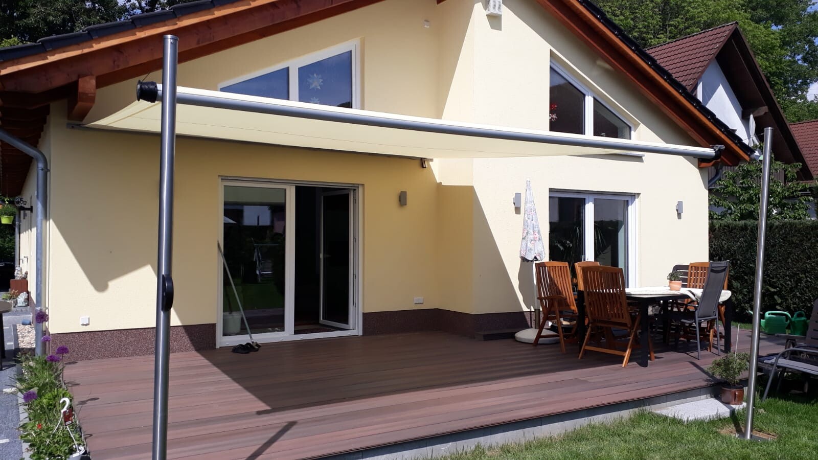 Gelbes Einfamilienhaus mit offener Terrassentür, Holzdeck, Esstisch, Stühle und Sonnenschirm.