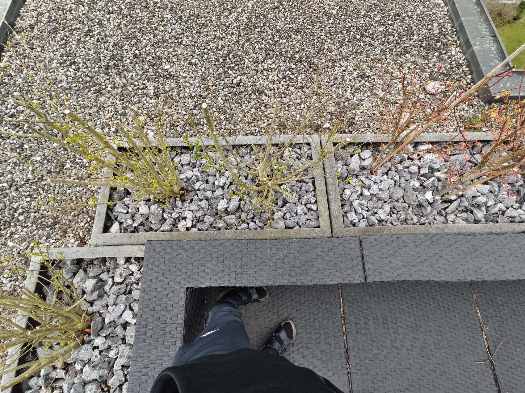 Von oben: Terrasse mit grauer Sitzgruppe, Kiesbeete und Sträuchern; Person steht auf der Sitzfläche.