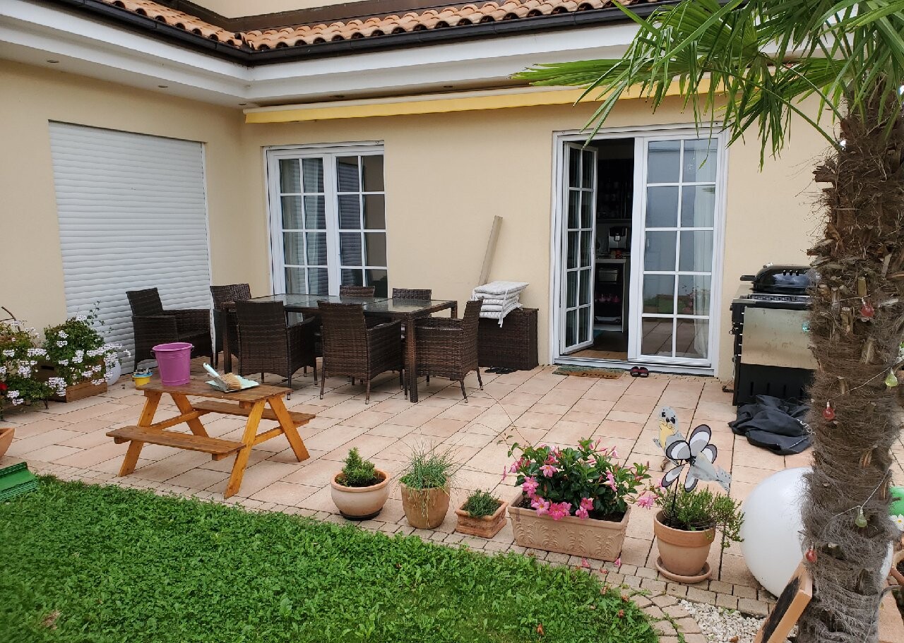 Garten-Patio mit Esstischgruppe aus Rattan, Pflanzkübeln, Grill und offenen Glastüren.