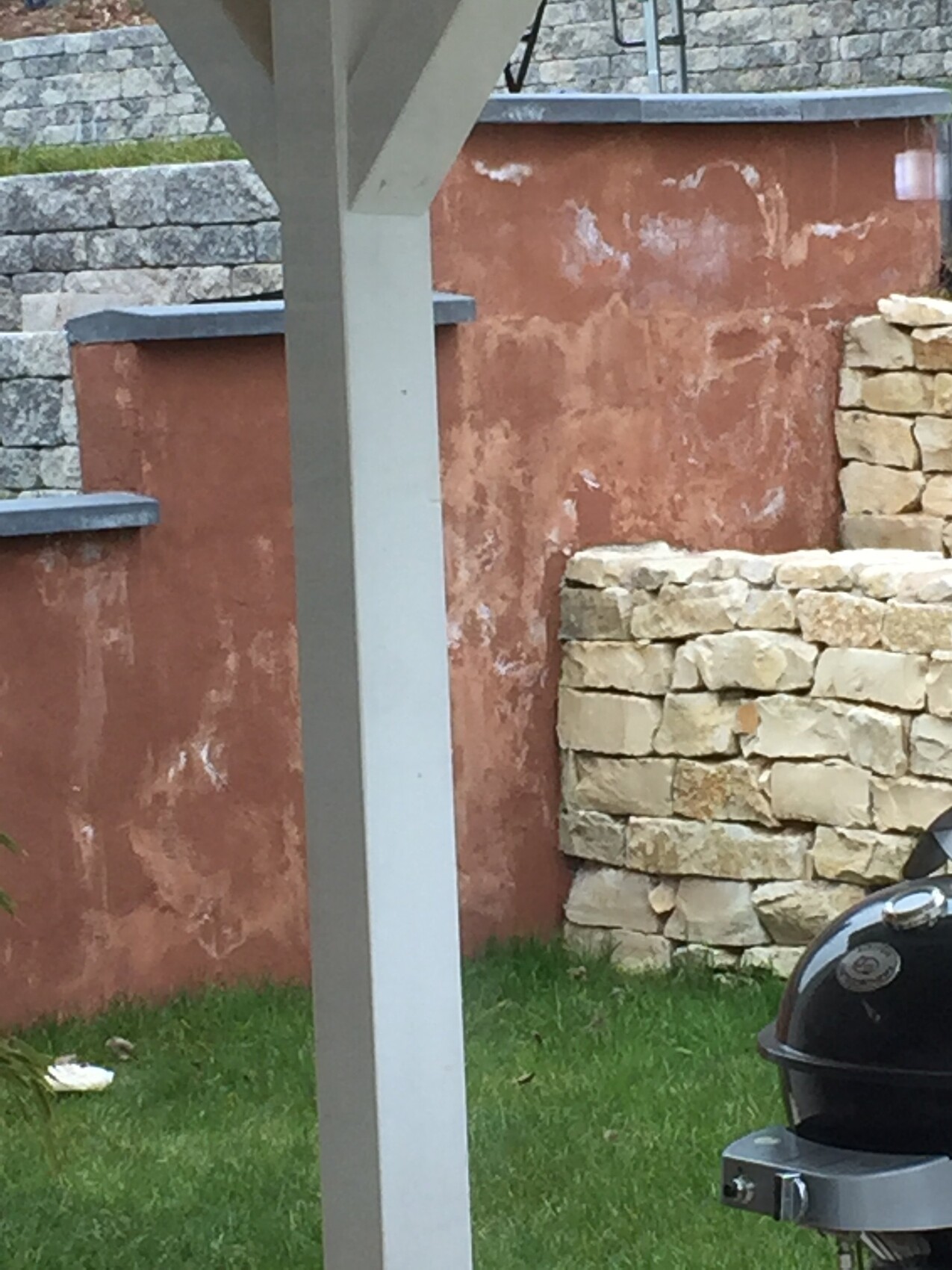 Außenbereich mit Grill, roter Verputzwand und Steinmauer im Garten.