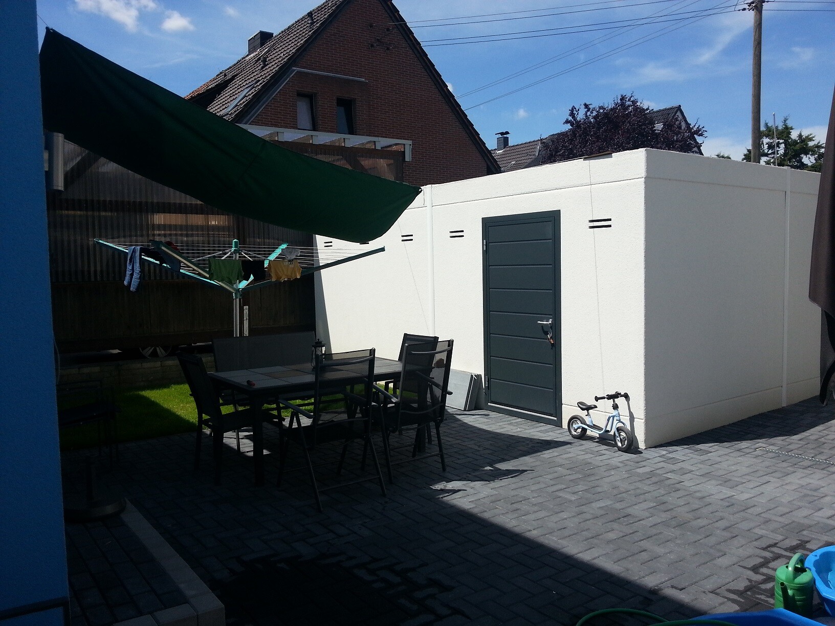 Hof mit Esstisch und Stühlen, Wäscheleine, grünem Sonnensegel, weiße Betonwand, Kinderfahrrad