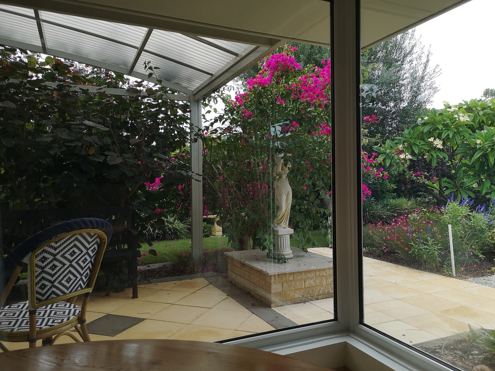Terrasse mit Garten, Bougainvillea, Statue und Brunnen hinter Glasfront
