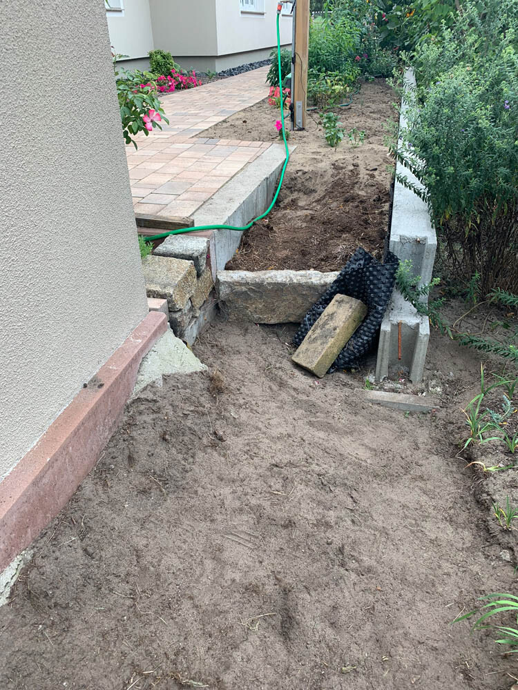 Gartenbaustelle: Erdarbeiten, Pflasterweg, grüner Schlauch neben Steinen