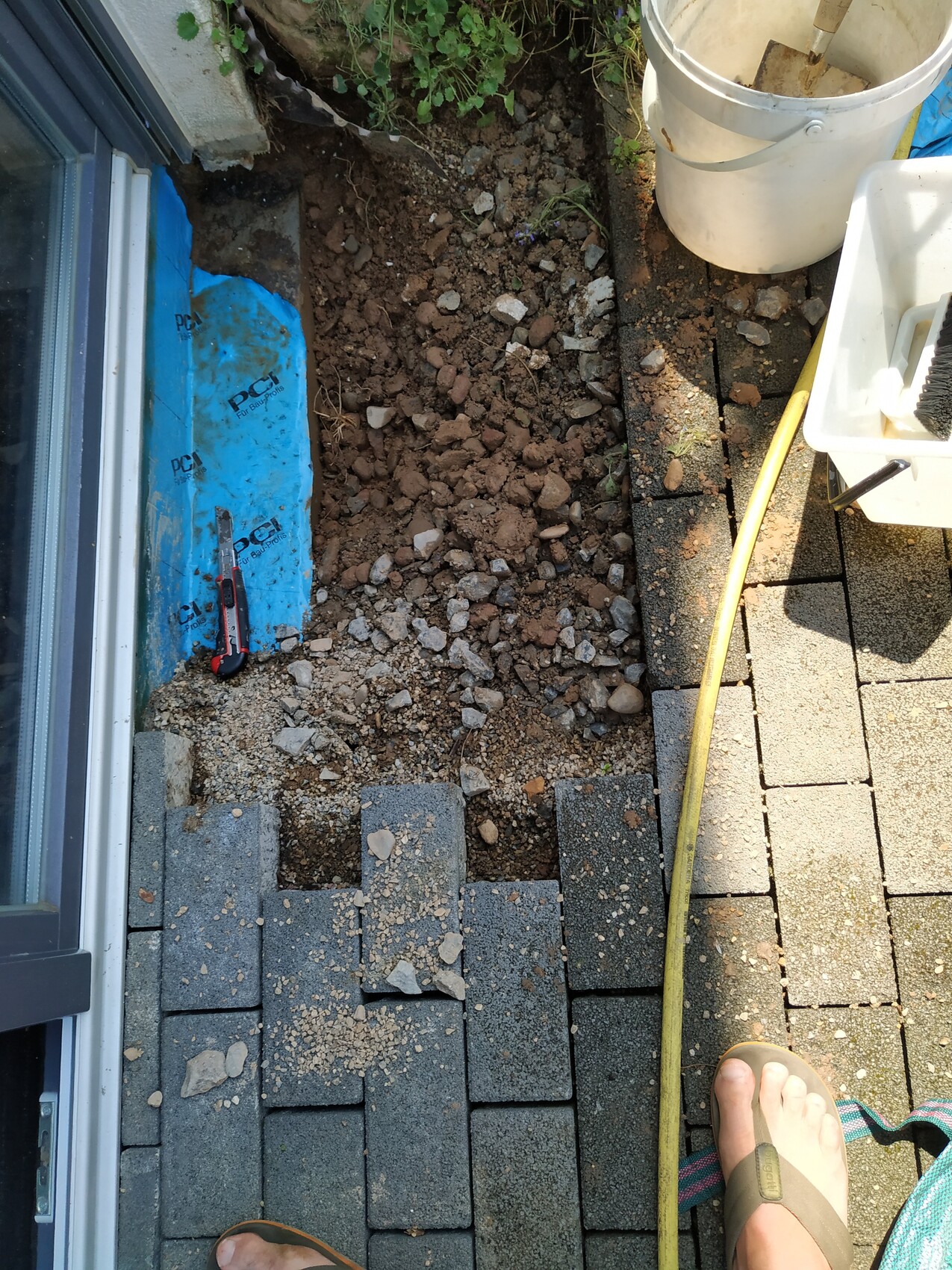 Außenbereich einer Terrasse mit Pflastersteinen, Erde, Kies und Bauwerkzeugen neben einer Tür