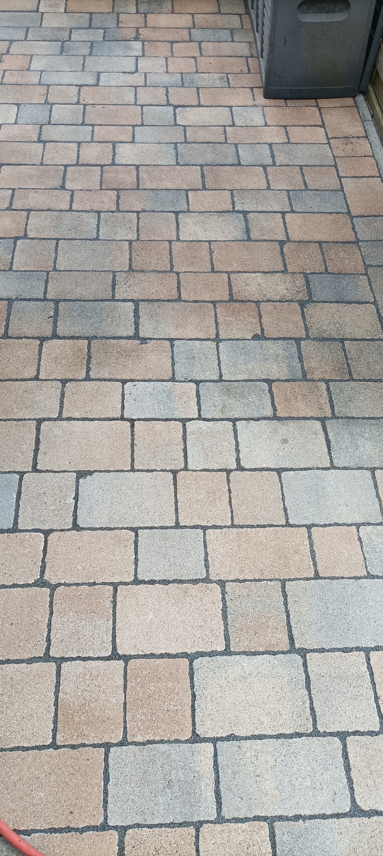 Gepflasterter Gehweg aus rechteckigen Steinen in Beige und Grau; rechts Mülleimer.