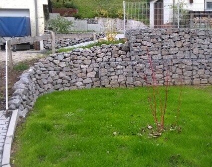 Garten mit steinernem Hangmauer, Grasfläche und kleinem Baum