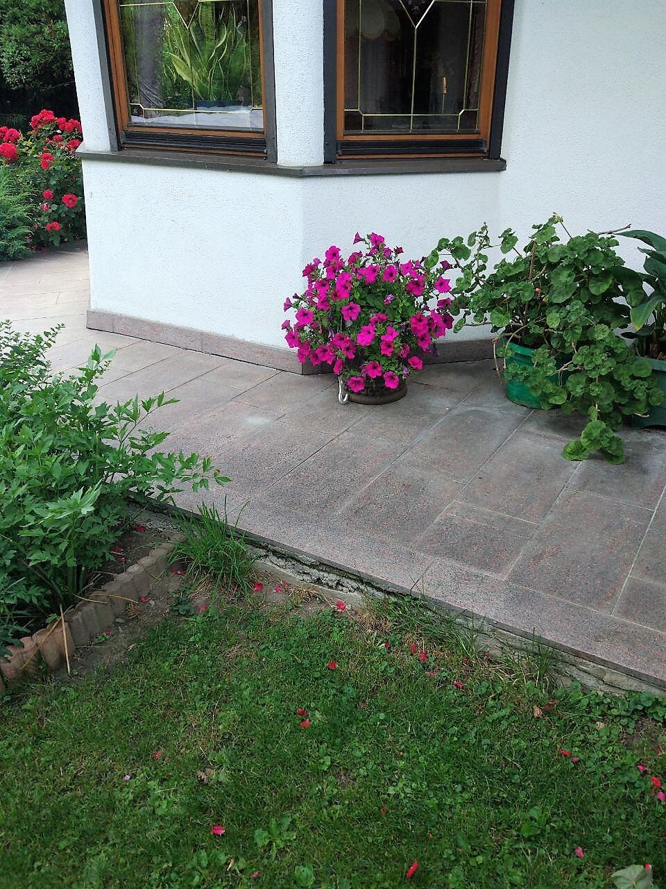 Weiße Hauswand mit braunen Fensterrahmen, bunte Blumenkübel vor der Terrasse