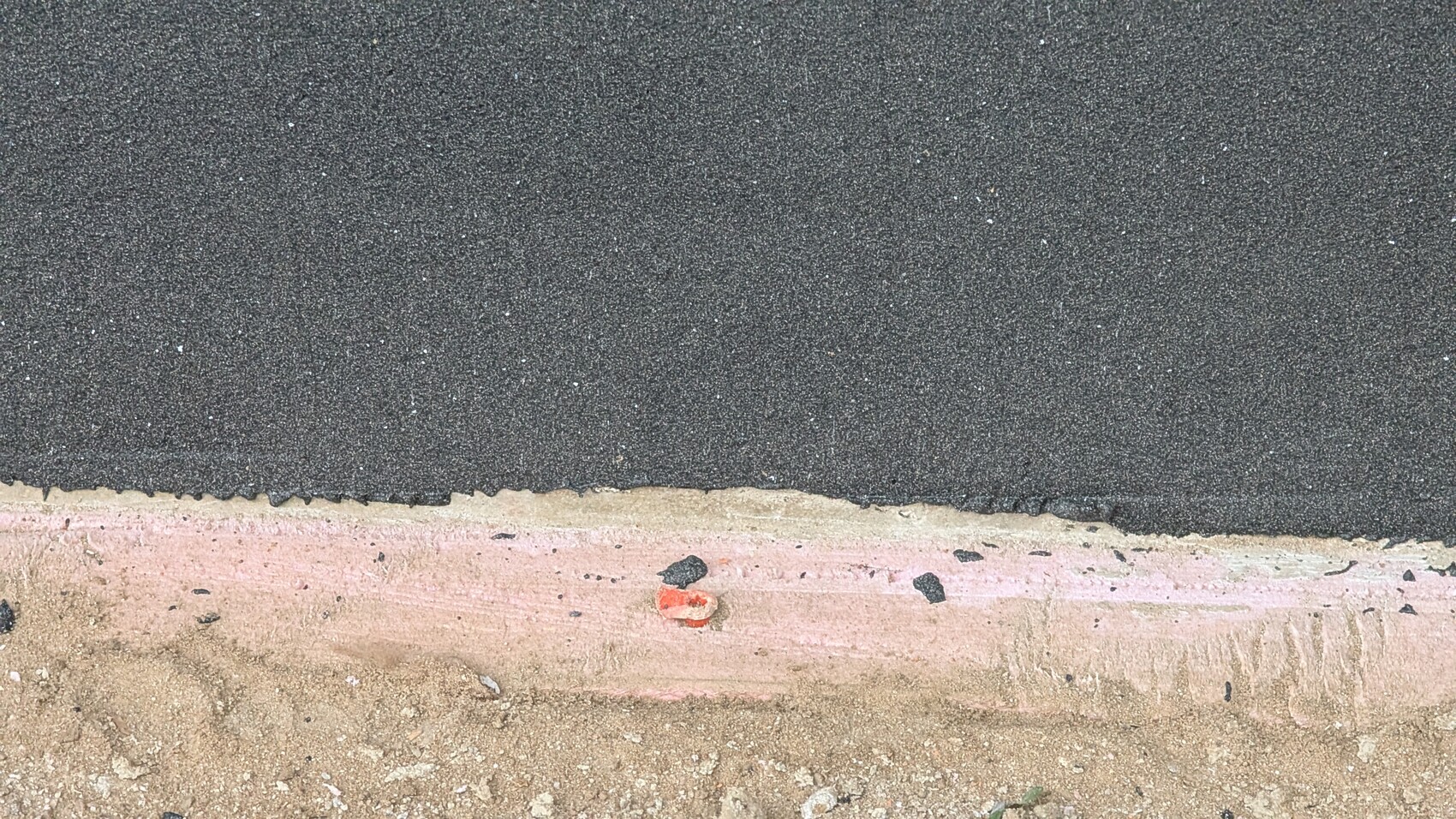 Außenbereich mit dunklem Asphaltbelag und pinkem Rand am Vorplatz.
