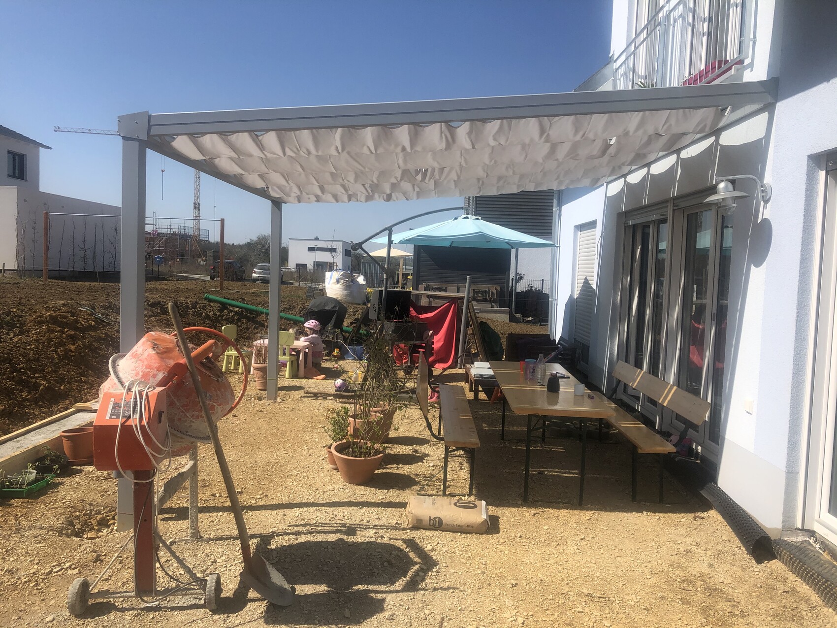 Außenbereich eines Hauses mit Pergola, Tischgruppe, Spielzeug und Baugeräten