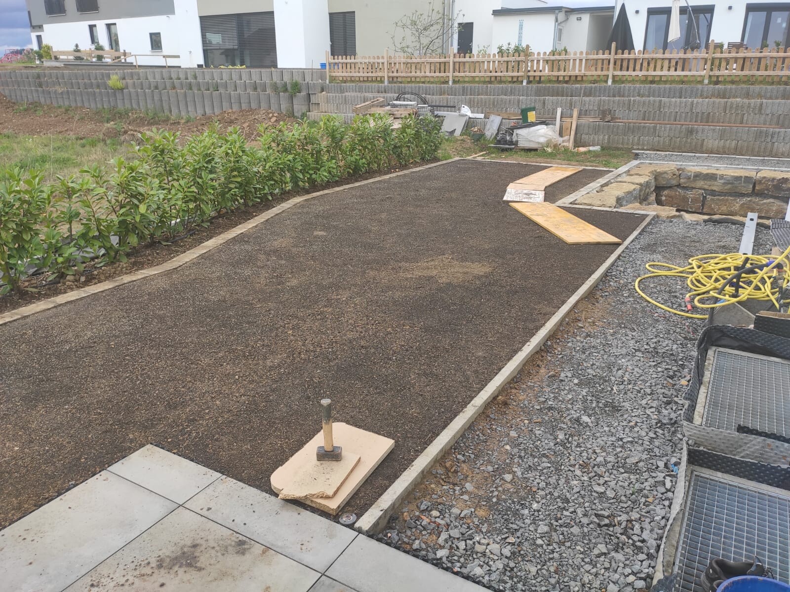 Gartenweg mit Kiesbelag, Holzrand und Bauwerkzeugen im Hintergrund