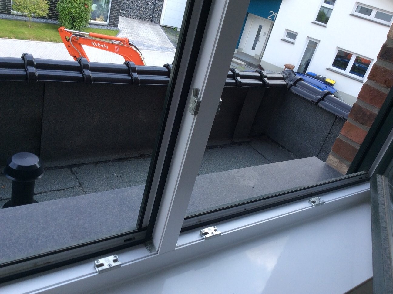 Blick vom Fenster auf Balkonterrasse mit grauer Plattenverkleidung und orangeem Bagger