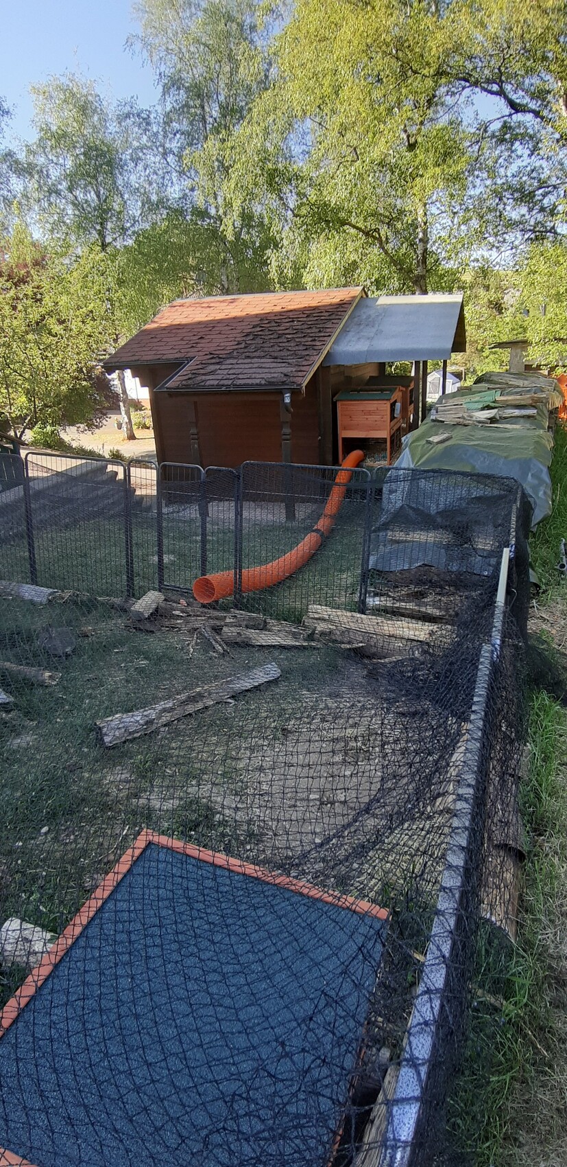 Kleines Gartenareal mit Holzhäuschen, Zaun und orangefarbenem Rohr auf einer Baustelle