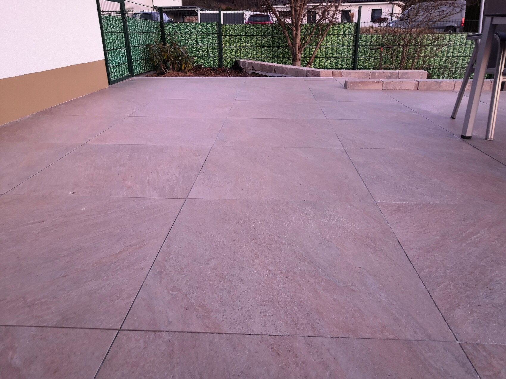 Große Steinoptik-Terrassenplatten auf offener Terrasse mit Gartenzaun.