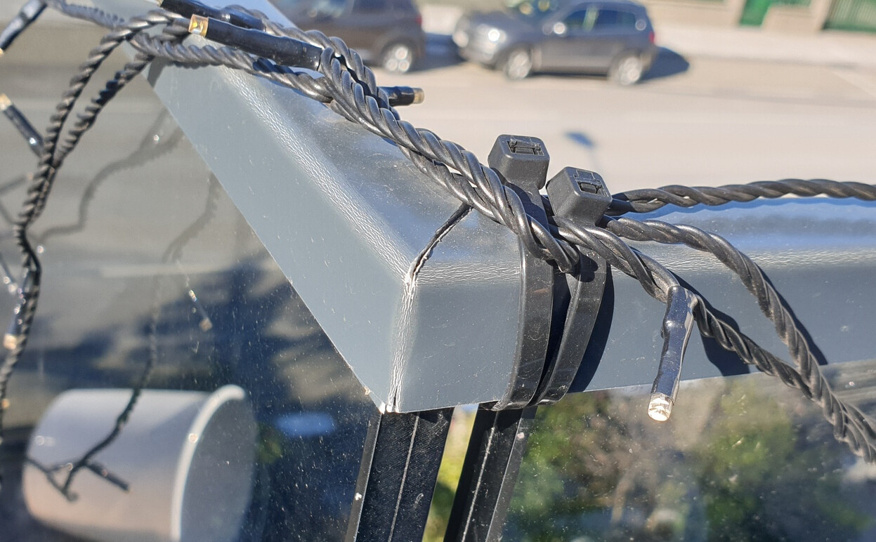Nahaufnahme eines Geländers mit Drahtseilen und Halterung; Parkplatz im Hintergrund.