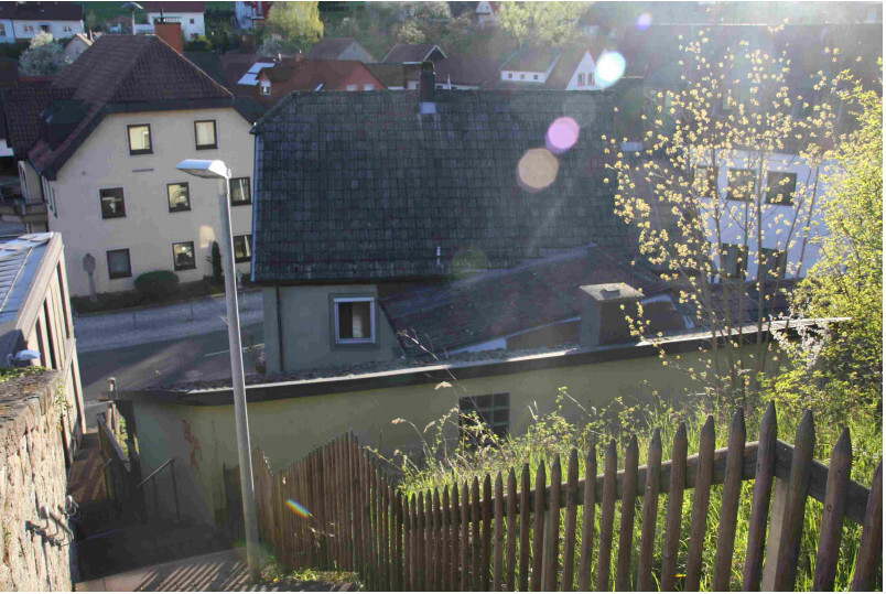 Außenaufnahme eines Wohnviertels mit Holzzaun, Treppe und Häusern im Hintergrund, Sonnenschein