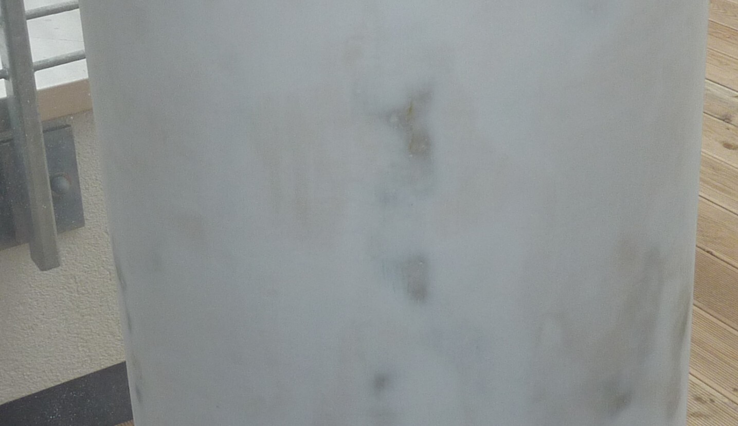 Außenbereich mit Holzdeck und grauem Wandpaneel, Geländer im Hintergrund.