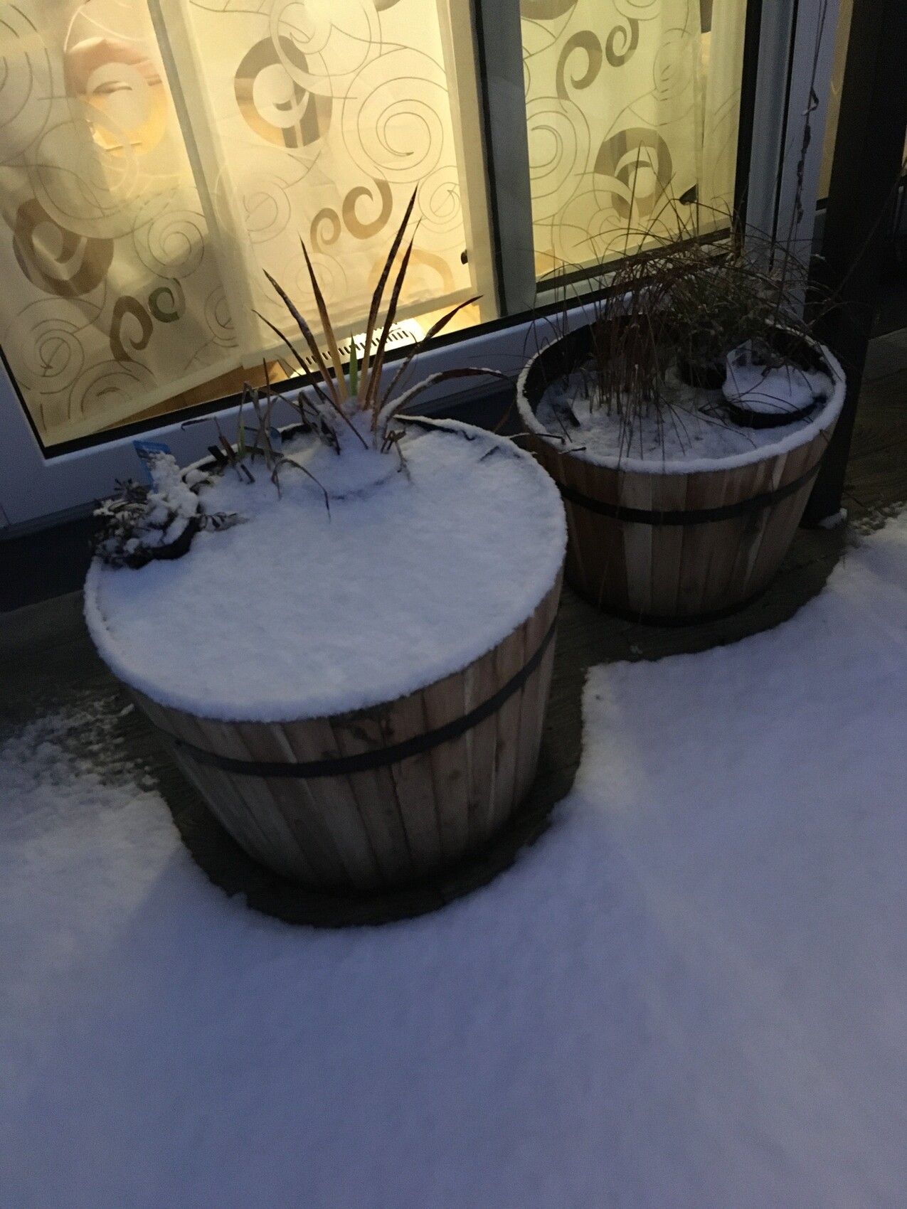 Zwei runde Holz-Pflanzkübel mit Schnee vor Glasfassade im Winter.