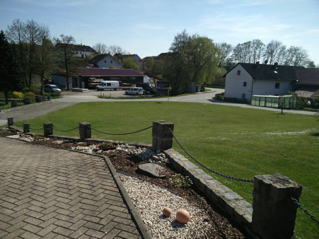 Sonniger Gartenbereich mit Terrasse, Steinpfosten, Kette und Häusern im Hintergrund