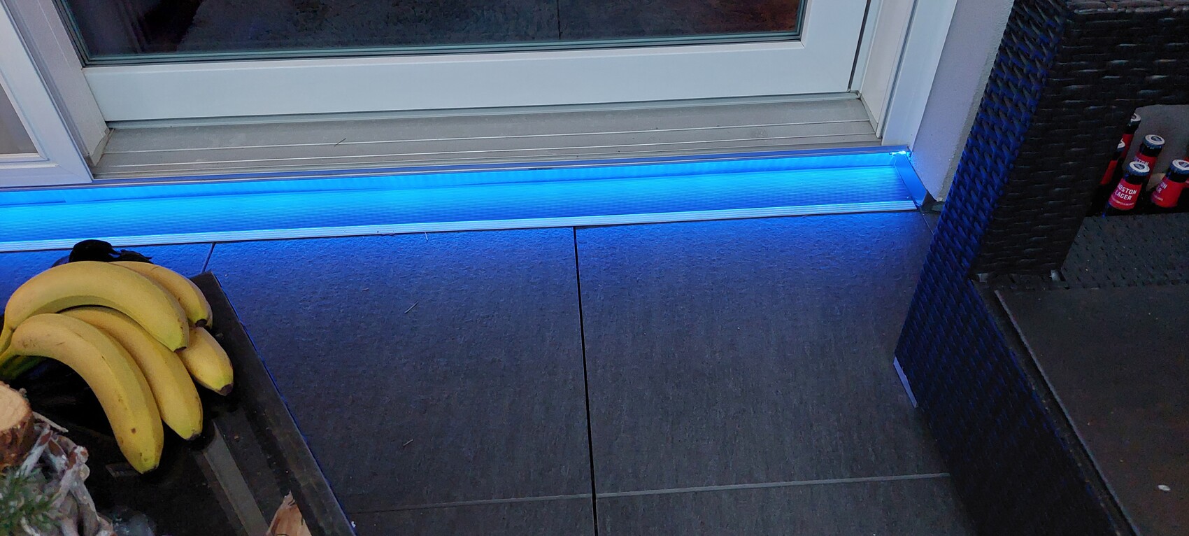 Bananen links, blaue LED-Lichtleiste an der Türschwelle, rechts Korbsessel und rote Dosen