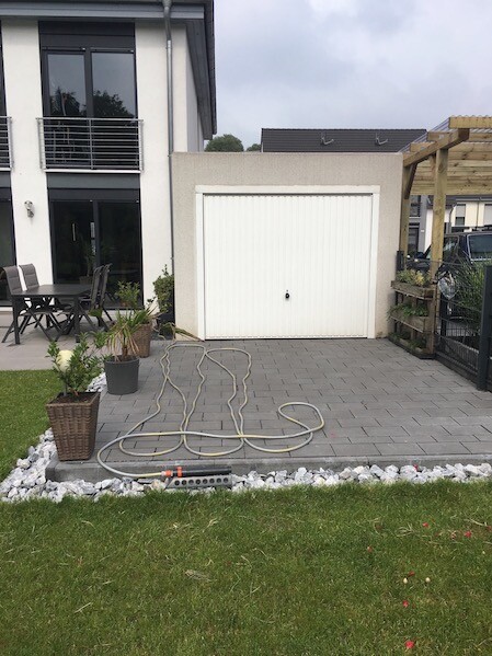 Moderne Hausfront mit Garage, gepflastertem Vorplatz, Gartenschlauch und Pflanzen