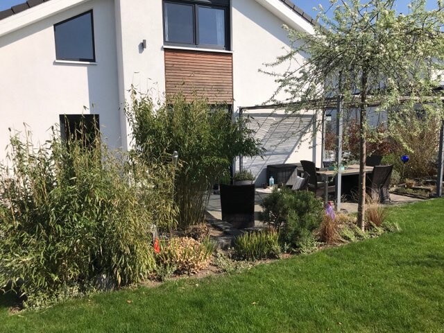 Außenansicht eines hellen Einfamilienhauses mit Terrasse, Garten und Sitzbereich.
